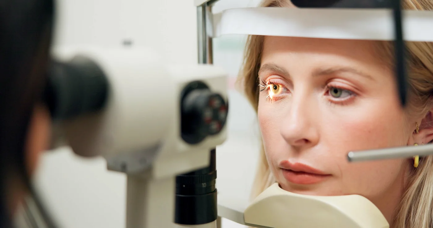 Optometrist performing an eye exam with a slit lamp in a well-lit examination room.